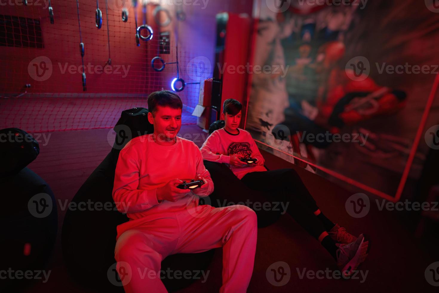 Father and son play gamepad video game console in red gaming room. Dad and kid gamers. photo