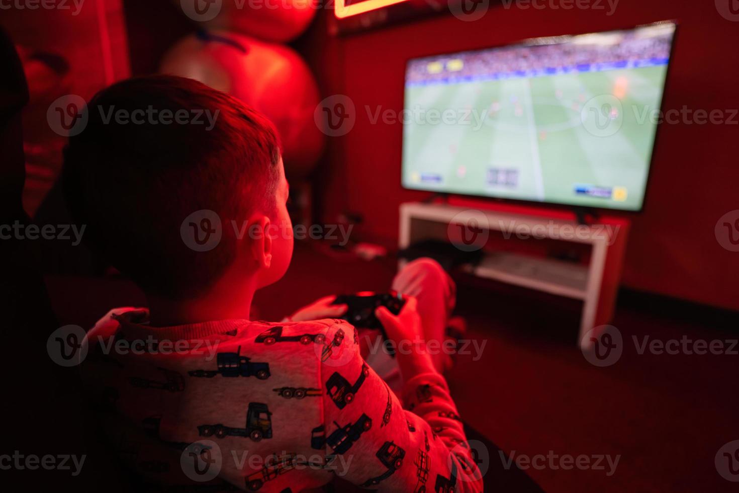 Boy gamer play gamepad football video game console in red gaming room. photo