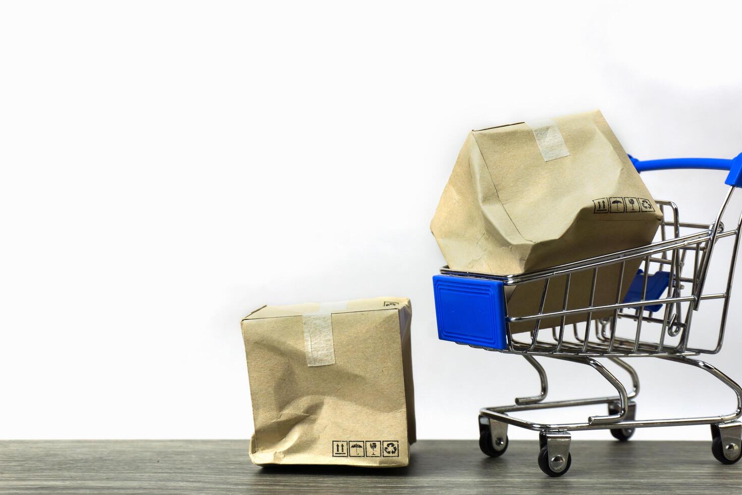 malo entrega conceptos. un dañado envase caja en pequeño azul compras carro modelo y en madera mesa con blanco antecedentes. foto