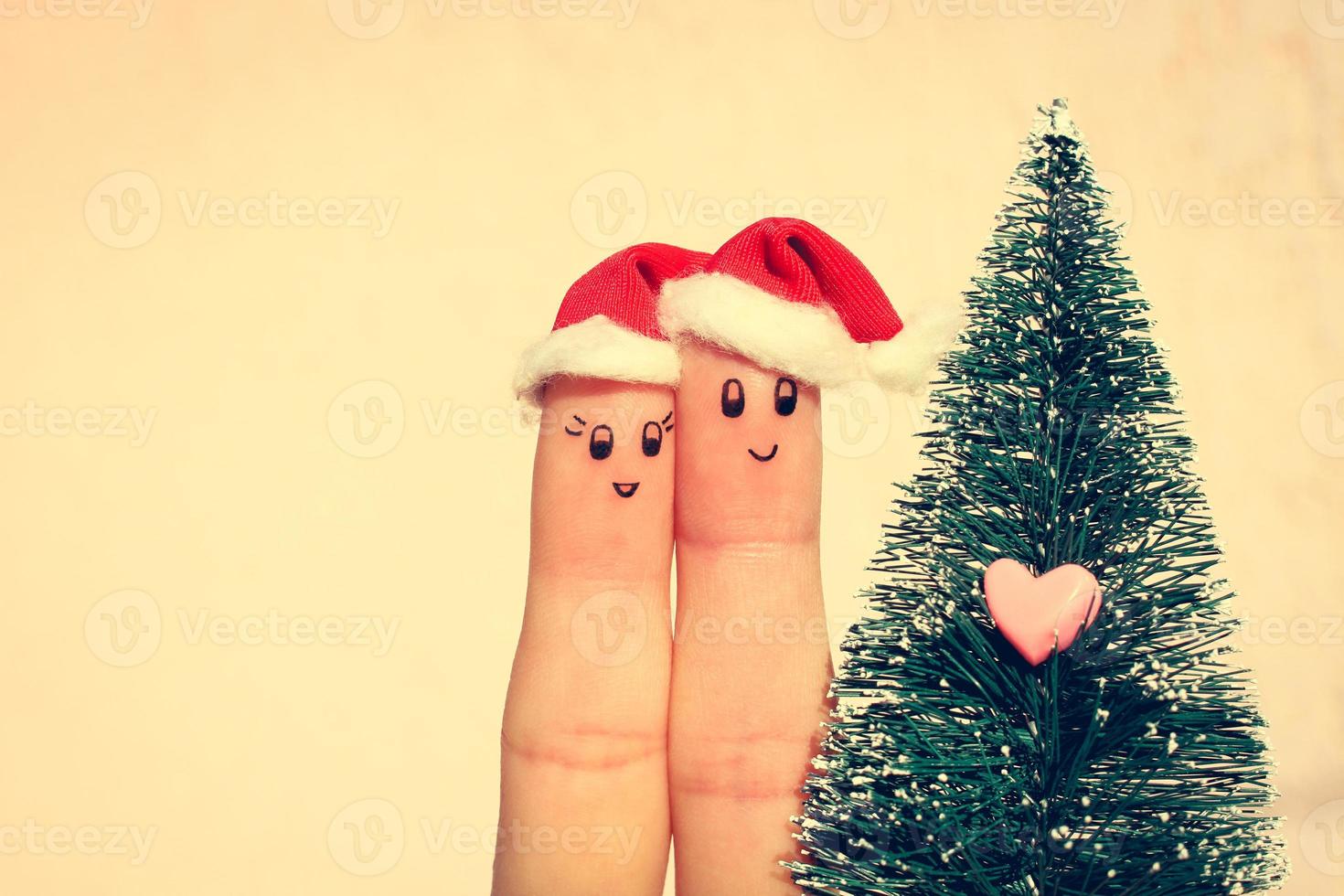 Finger art of couple celebrates Christmas. Concept of man and woman laughing in new year hats near Christmas tree. Toned image photo