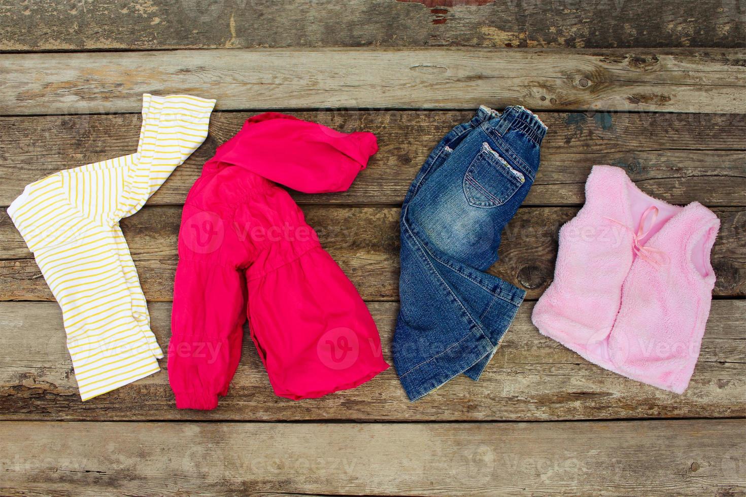 Children's clothing and accessories jeans, jacket, hair clips and warm vest on old wooden background. Top view. photo