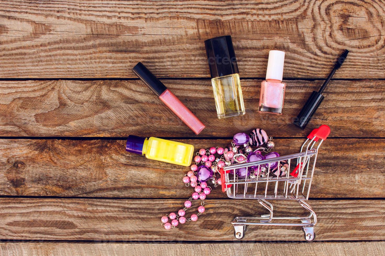 Shopping cart with cosmetics, beads on the old wood background. Toned image. photo