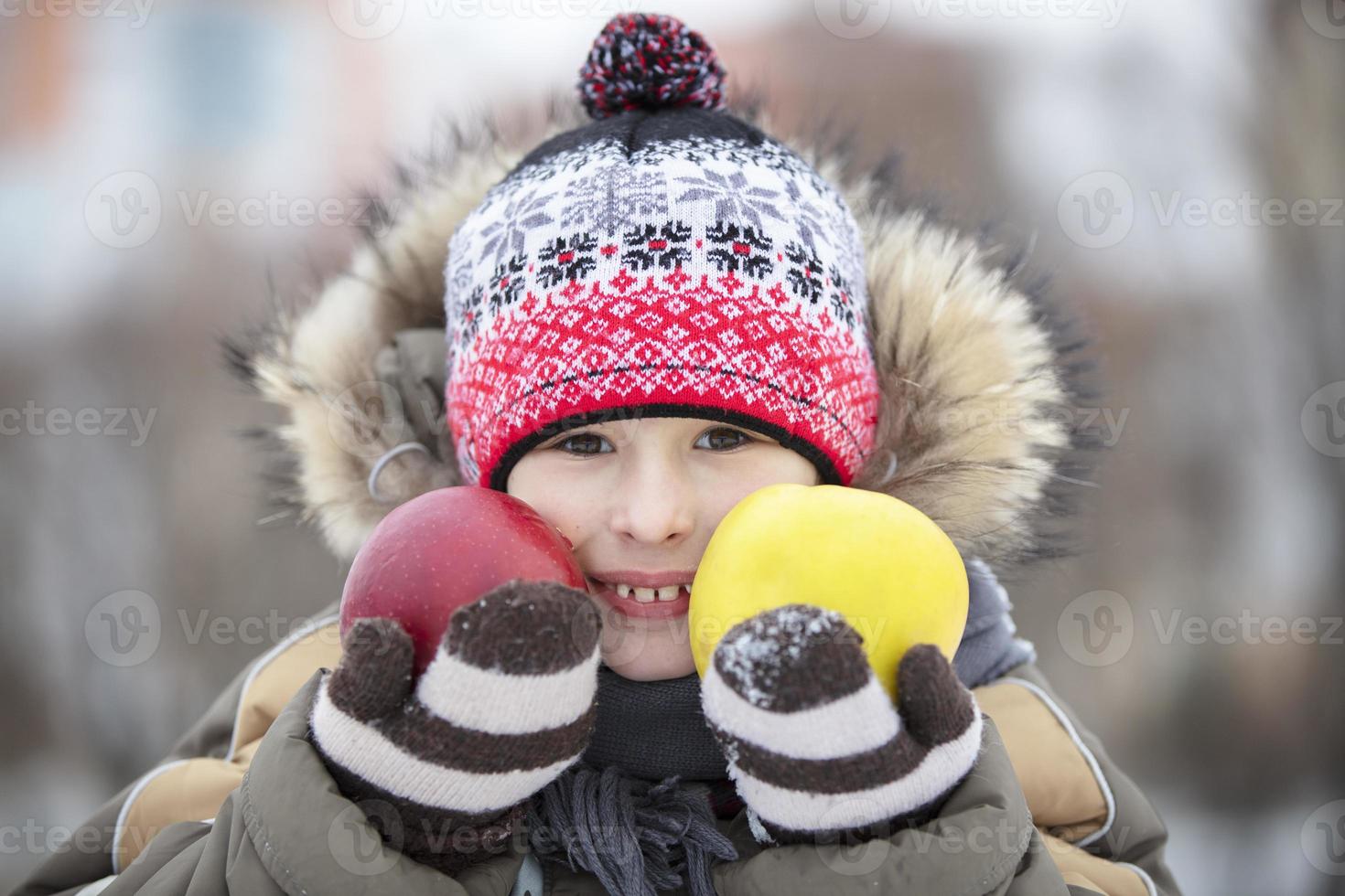 Child in the winter with fruit. The boy in the hat holds two large apples photo