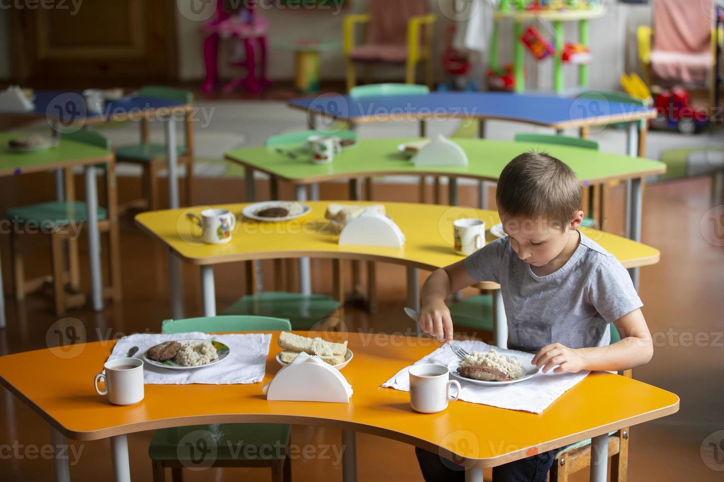 un niño come en jardín de infancia. un pequeño chico a el mesa con alimento. desayuno para niños. foto