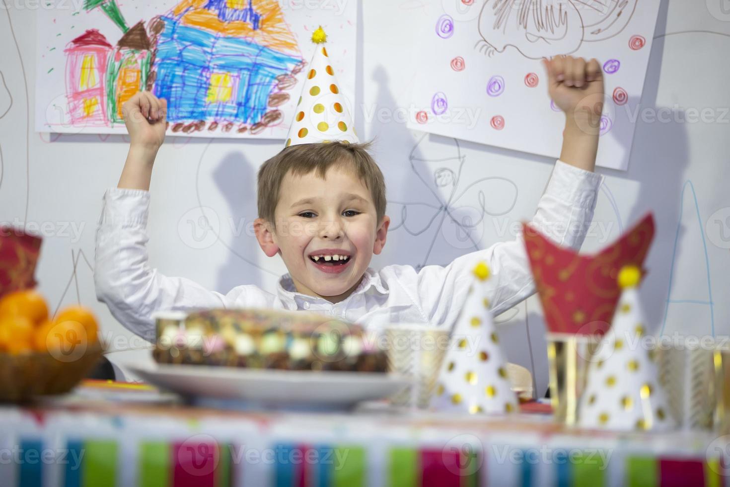 Happy birthday child. The boy at the festive table with a cap. photo