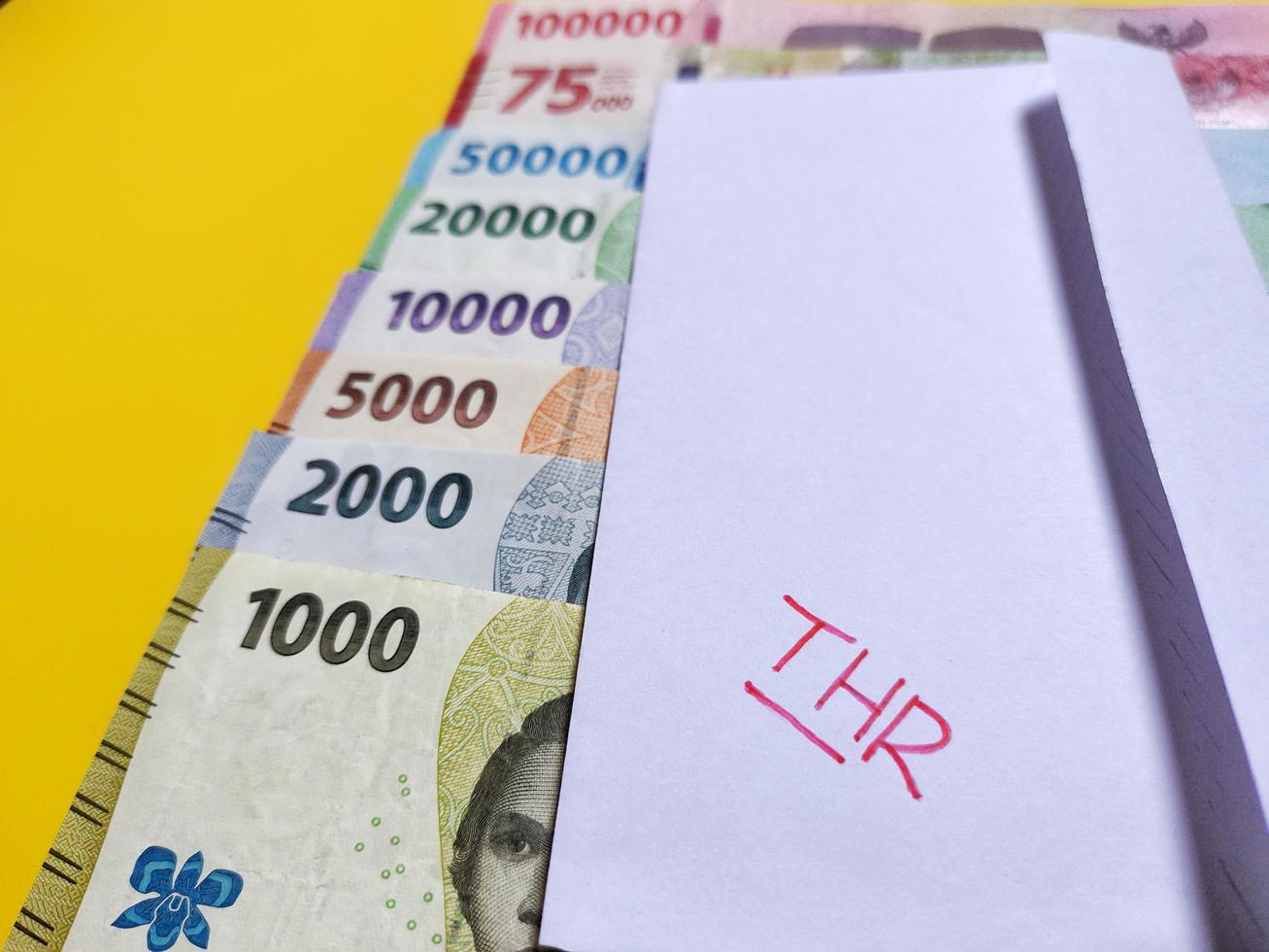 New banknotes issued in 2022 from Rp.1,000 to Rp.100,000. Indonesian rupiah currency with a white envelope labeled THR. Tunjangan Hari Raya concept isolated on yellow background photo