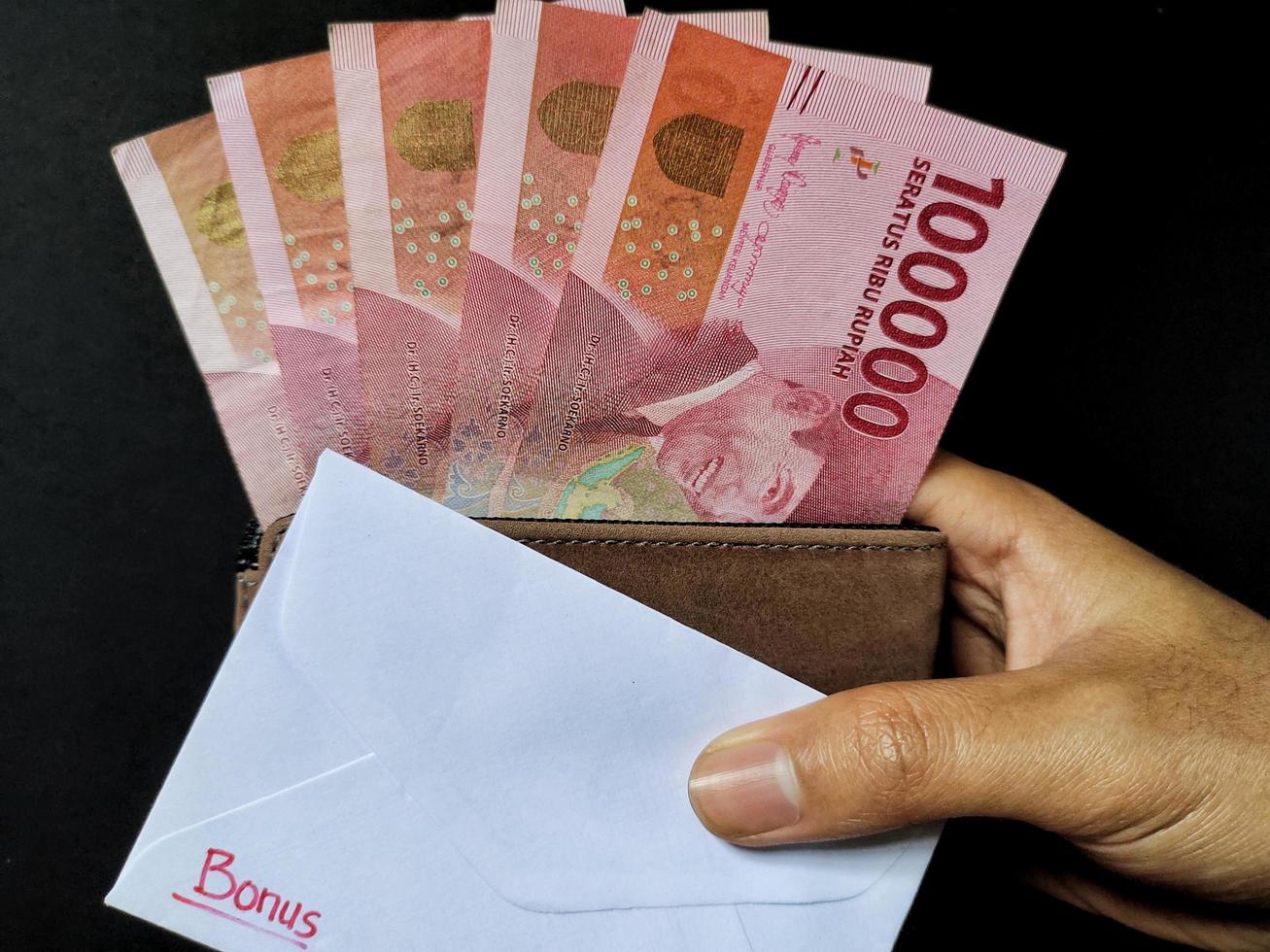 Man holding a white envelope written bonus and new Indonesian banknotes. Usually the Holiday Allowance or known as THR is given to employees ahead of Eid. Top view photo