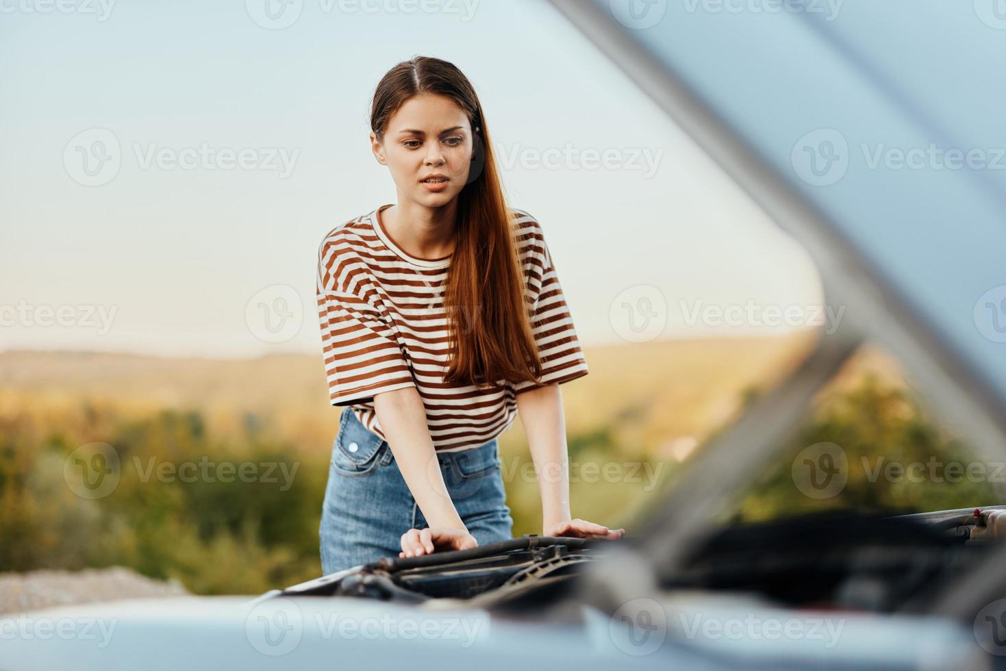 A sad woman has opened the hood of a broken down car and is looking for the cause of the breakdown on a road trip alone photo