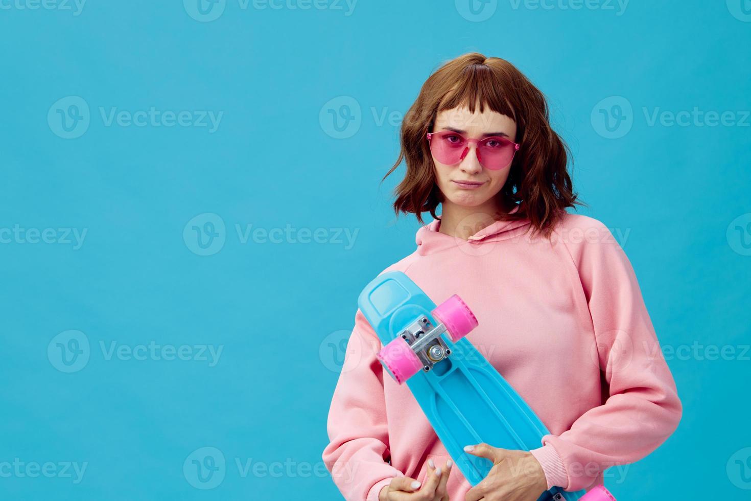 gracioso alegre bonito pelirrojo dama en rosado capucha Gafas de sol con centavo tablero sonriente posando aislado en azul estudio antecedentes. Copiar espacio bandera oferta. Moda cine. fiesta actividad foto