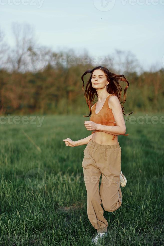 A woman of athletic build runs through the park on the green grass with loose, flying hair and working out into the sunset light photo
