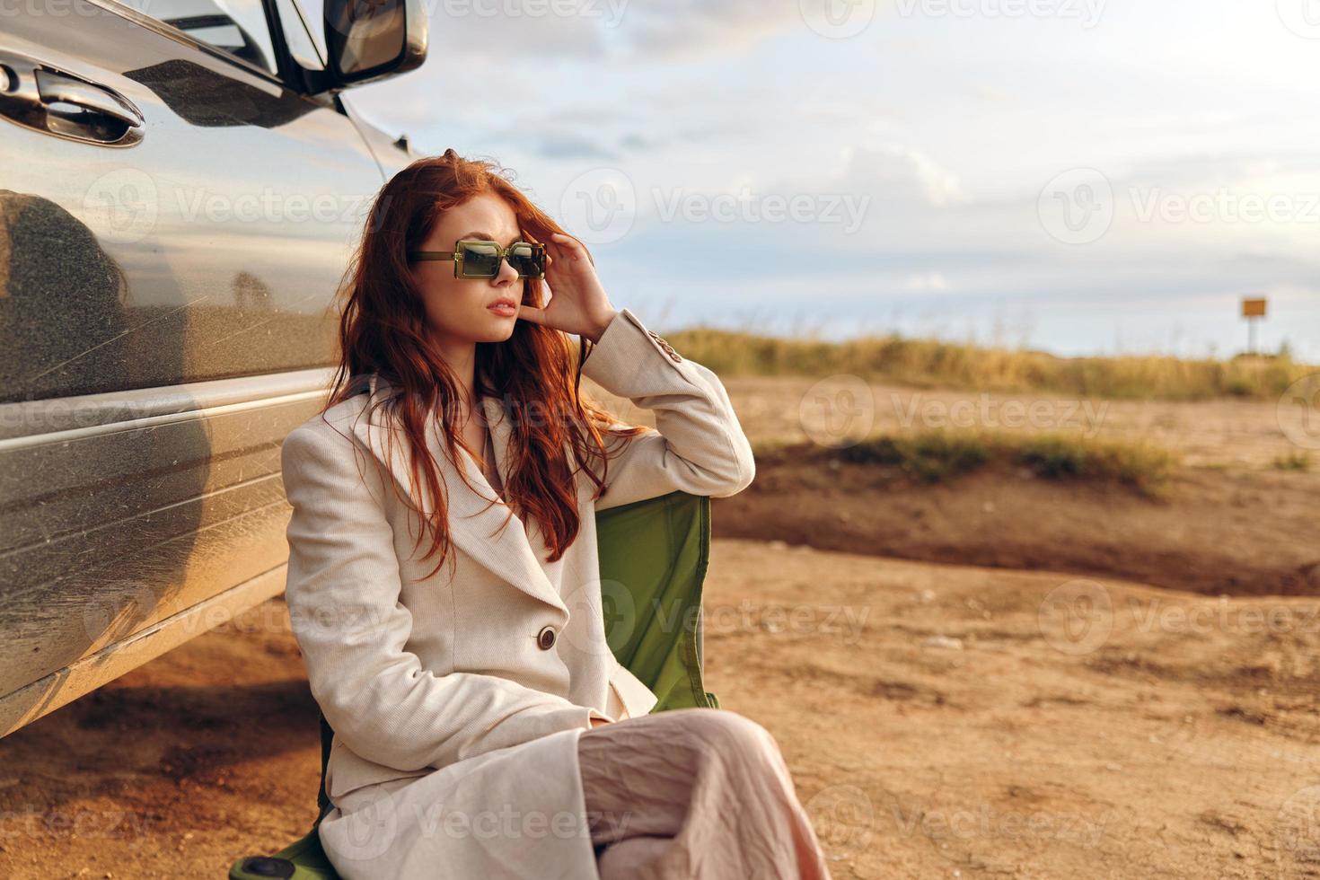 bonito mujer en un Saco al aire libre sentado en un silla cerca el coche cosecha foto