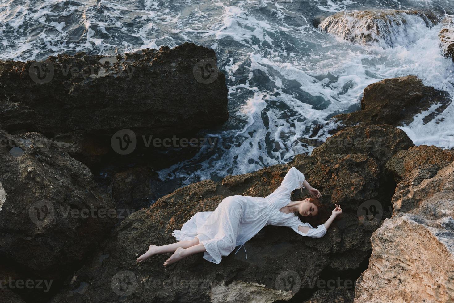Beautiful bride in long white dress wet hair lying on a rocky cliff Summer vacation concept photo