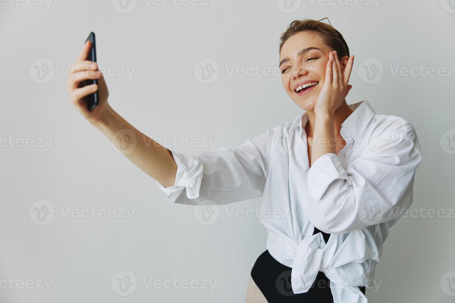 Teenage girl blogger takes photos and shoots. herself on video on her phone for social media content, video blogger, selfies against a white wall with a smile at home, freelancer