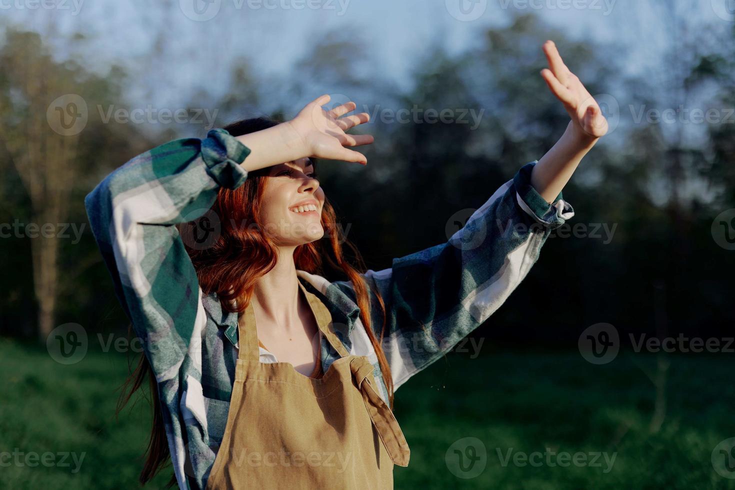 Portrait of a beautiful young woman with red hair in nature in a park in the summer, looking at the sunset against a background of green grass and trees photo