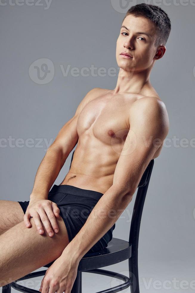 handsome guy with muscular body sitting on chair posing isolated background photo