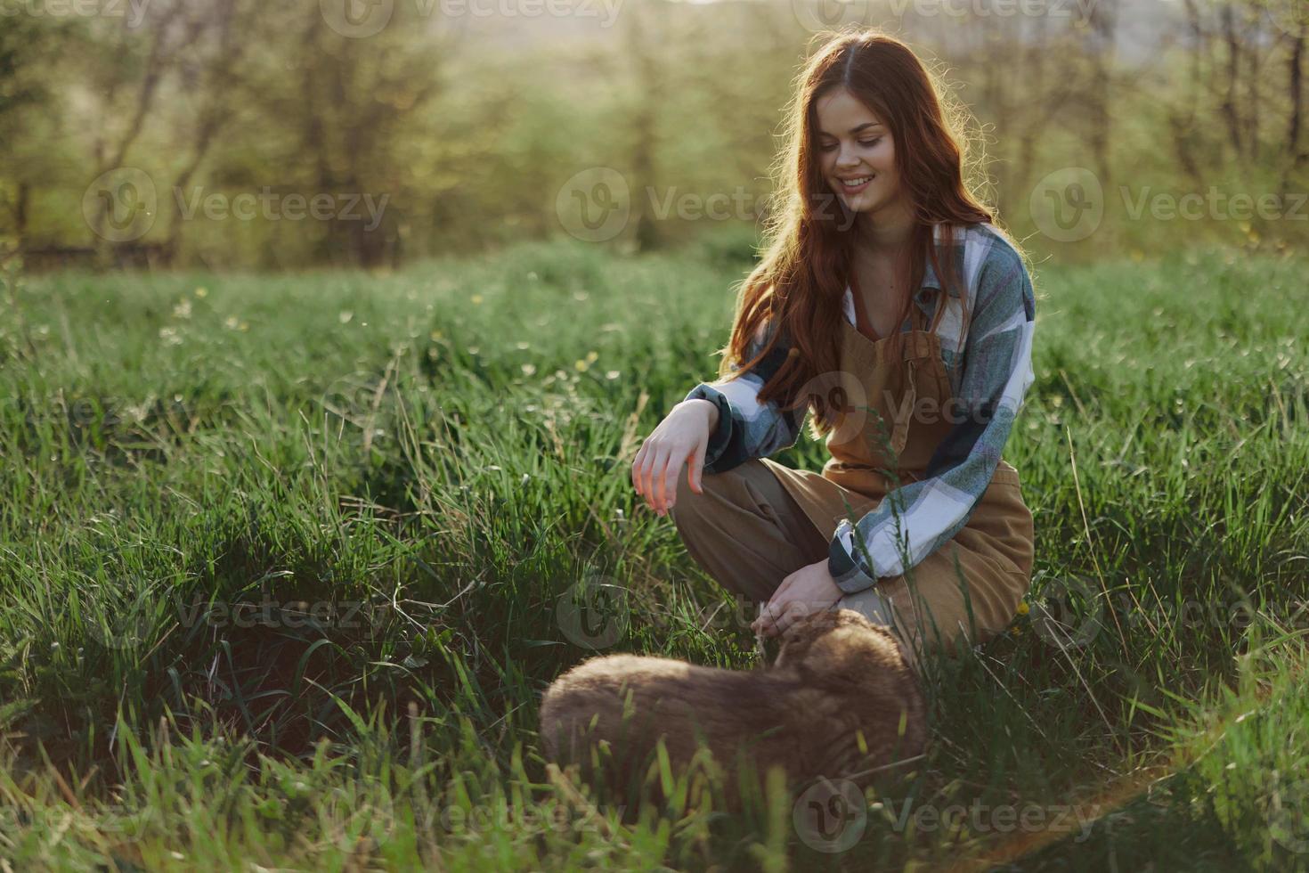 Young redheaded woman playing in nature with her dog in sunny park at sunset in summer photo