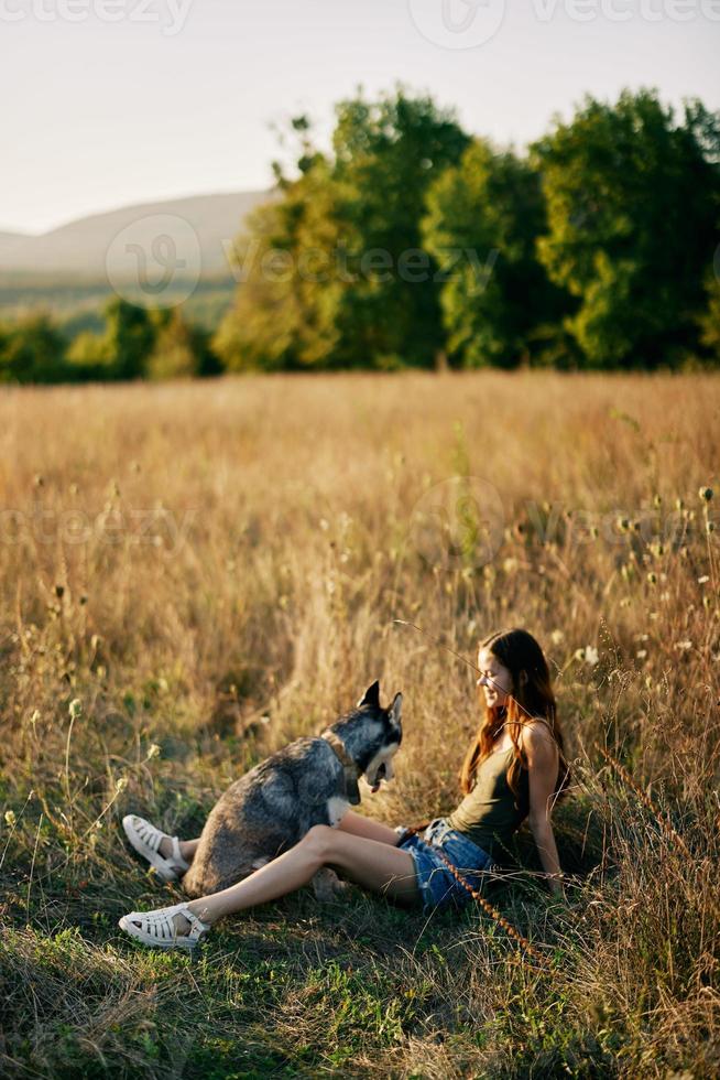 Woman sitting in a field with a dachshund dog smiling while spending time in nature with a friend dog in autumn at sunset photo