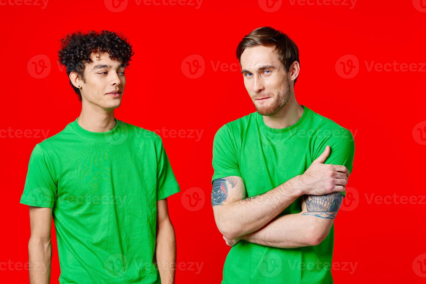 joyful friends in green t-shirts are standing next to red background photo