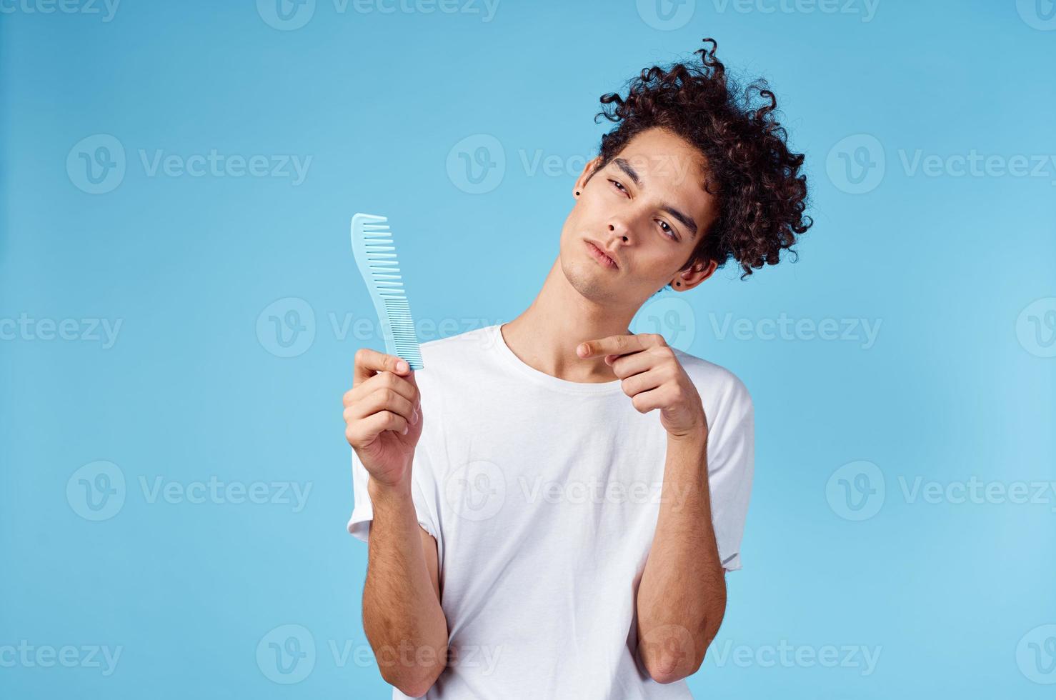 emotional man with a comb in his hand and curly hair in a blue background Copy Space photo