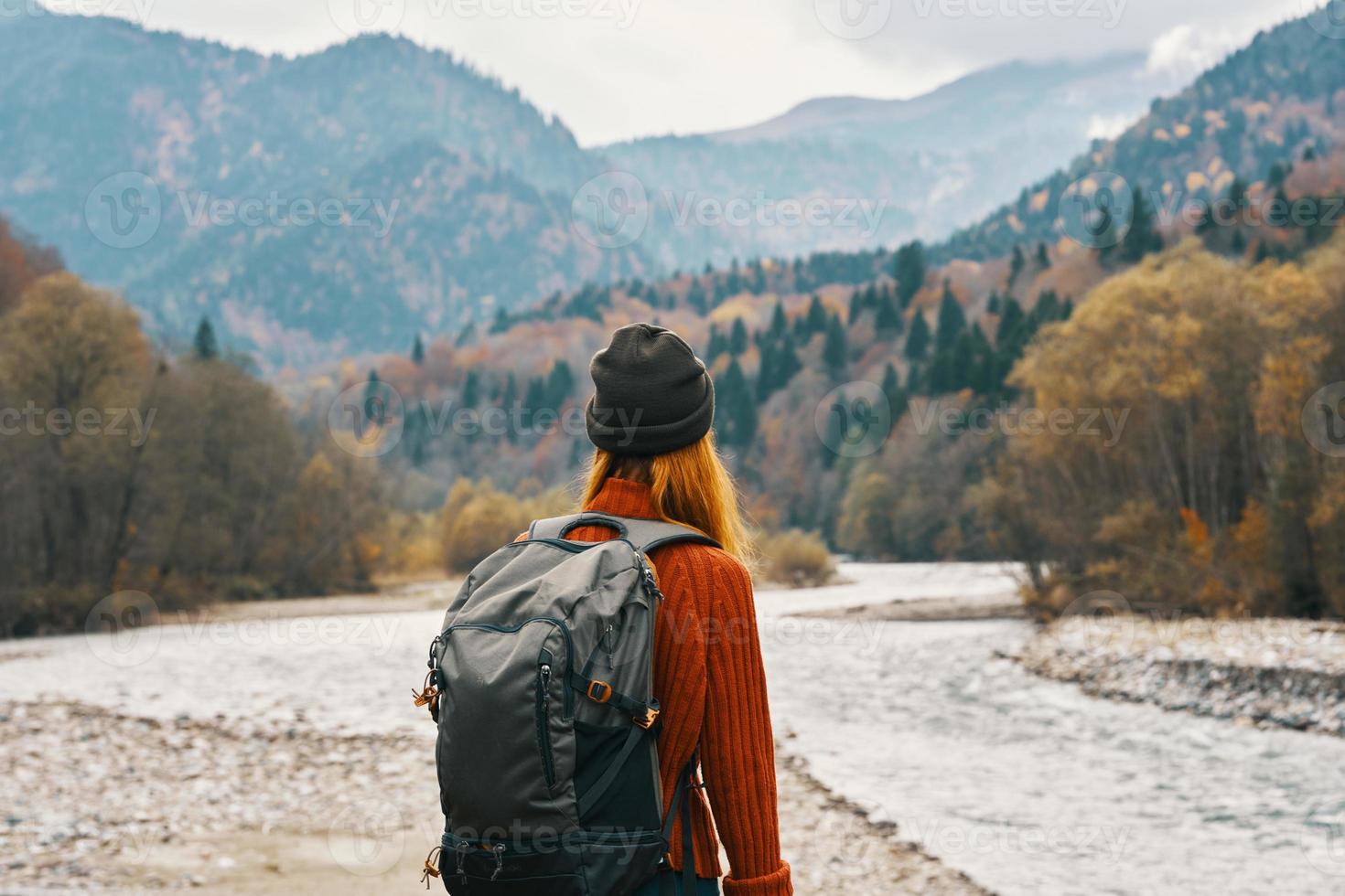 woman stands on the river bank and looks at the mountains in the distance landscape autumn backpack tourism model photo