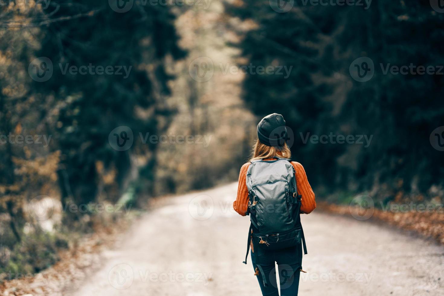 woman with a backpack in a hat and an orange sweater on the road in the autumn forest photo