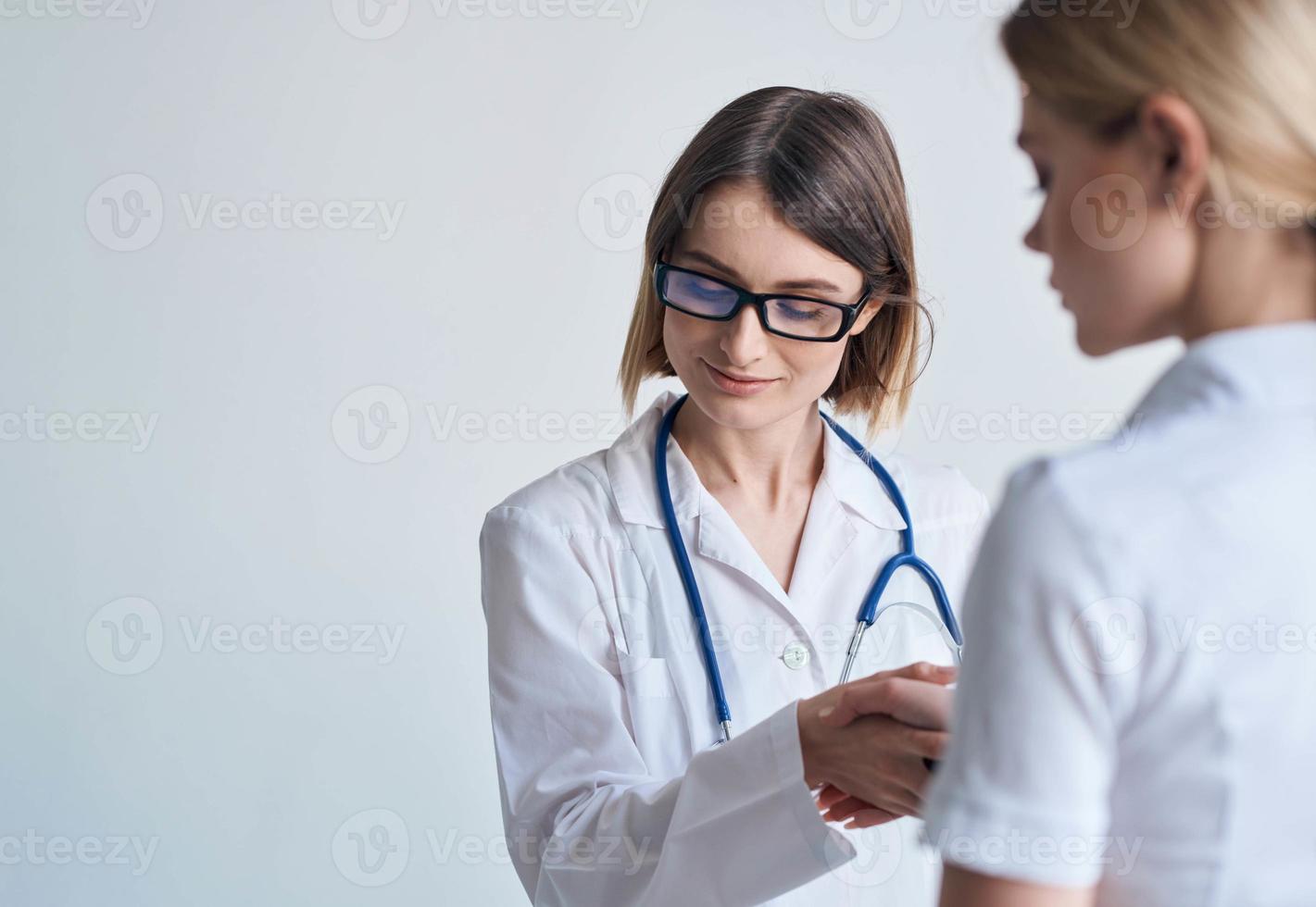 mujer médico en un médico vestido y lentes con un estetoscopio alrededor su cuello y un hembra paciente foto