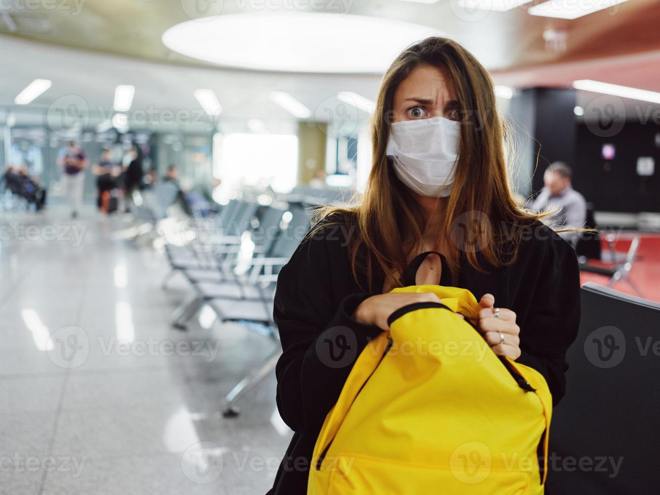 woman with wide open eyes medical mask yellow backpack airport photo