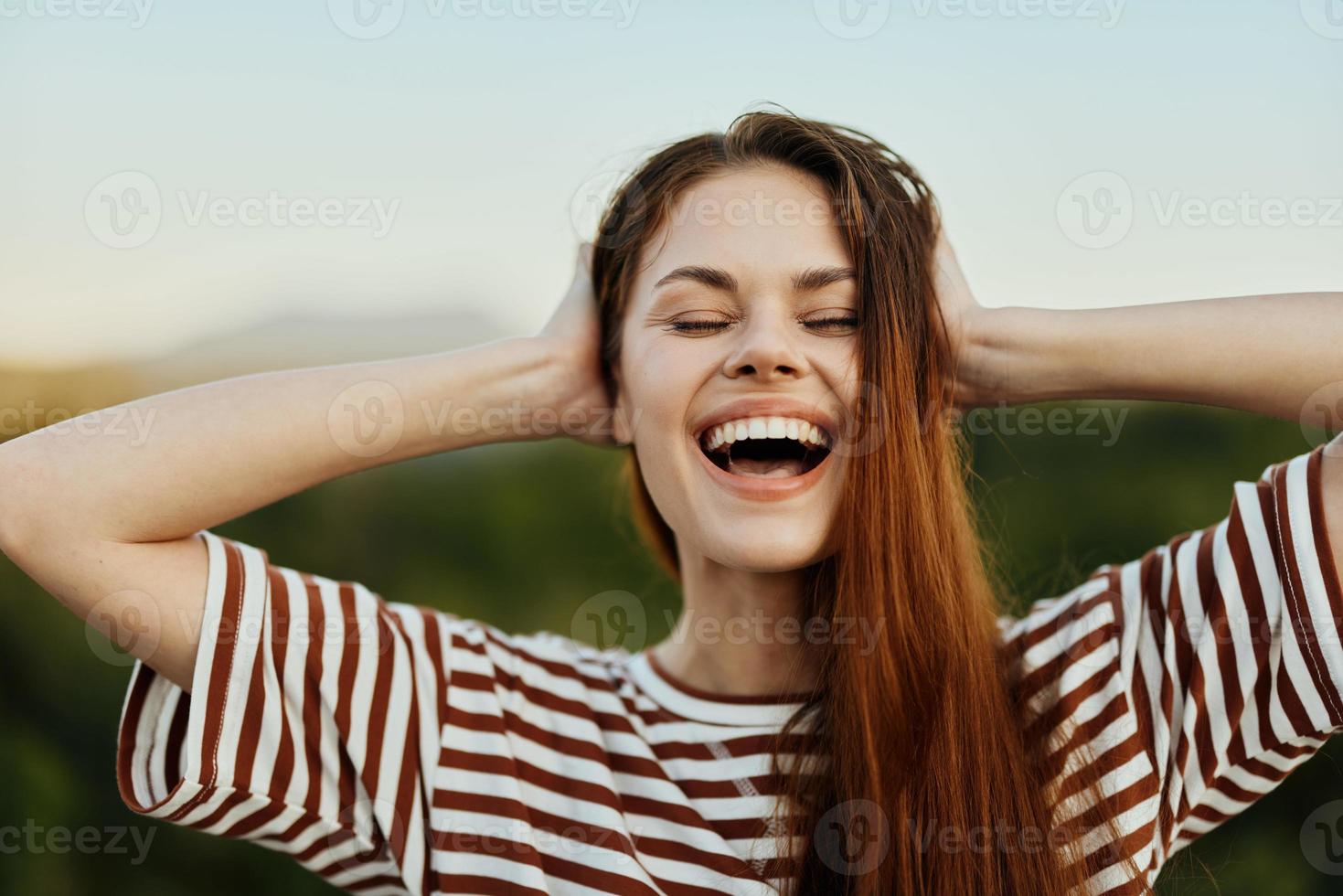 A young woman in a striped T-shirt sincerely laughs with her mouth open while traveling against the backdrop of autumn nature photo