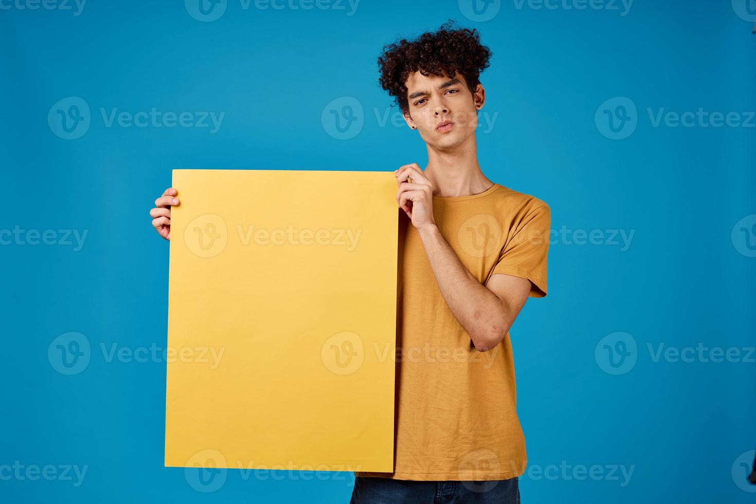 guy with curly hair yellow posters in hands Copy Space blue background studio photo