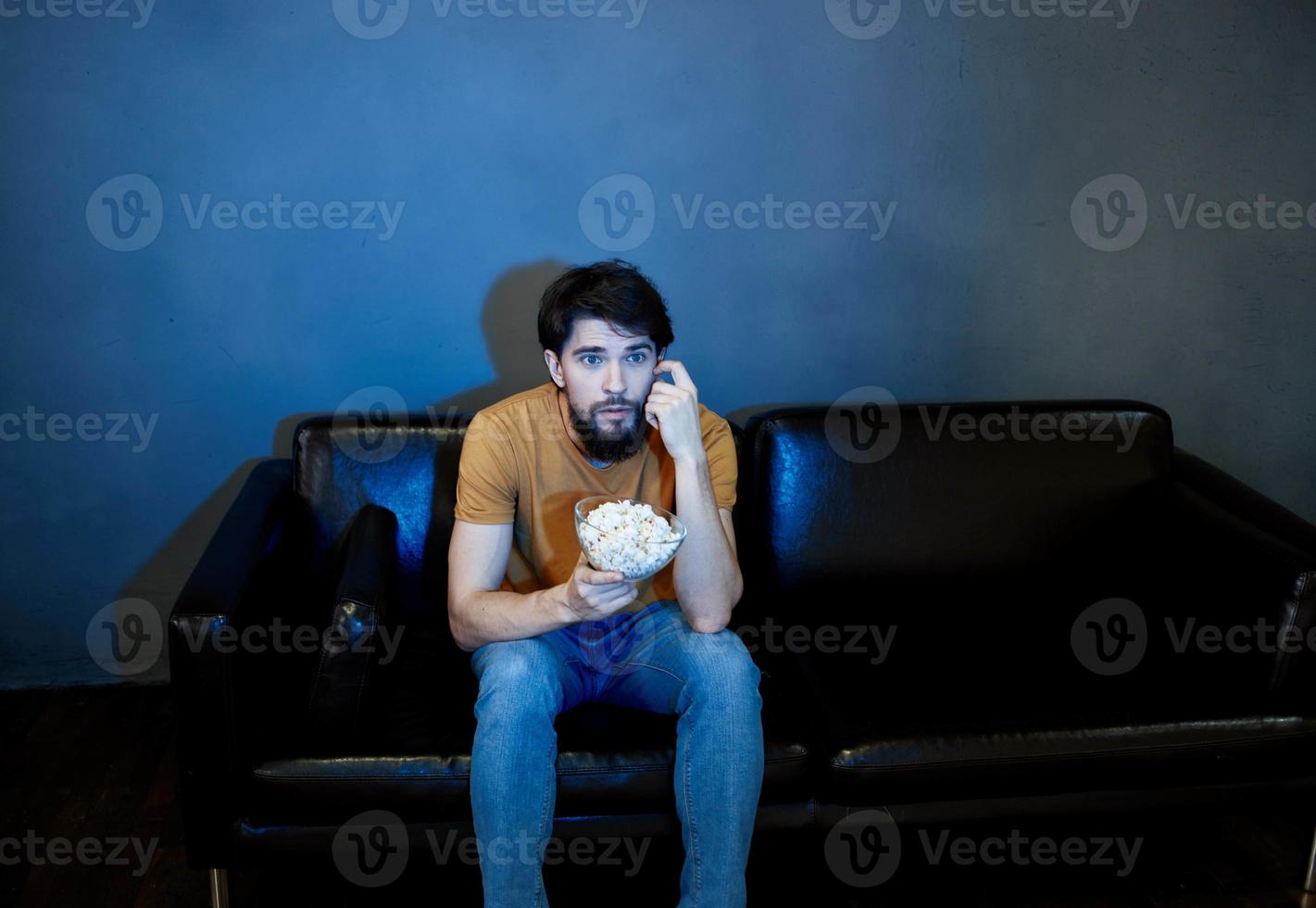 A man sits on a sofa indoors and watches TV front view photo