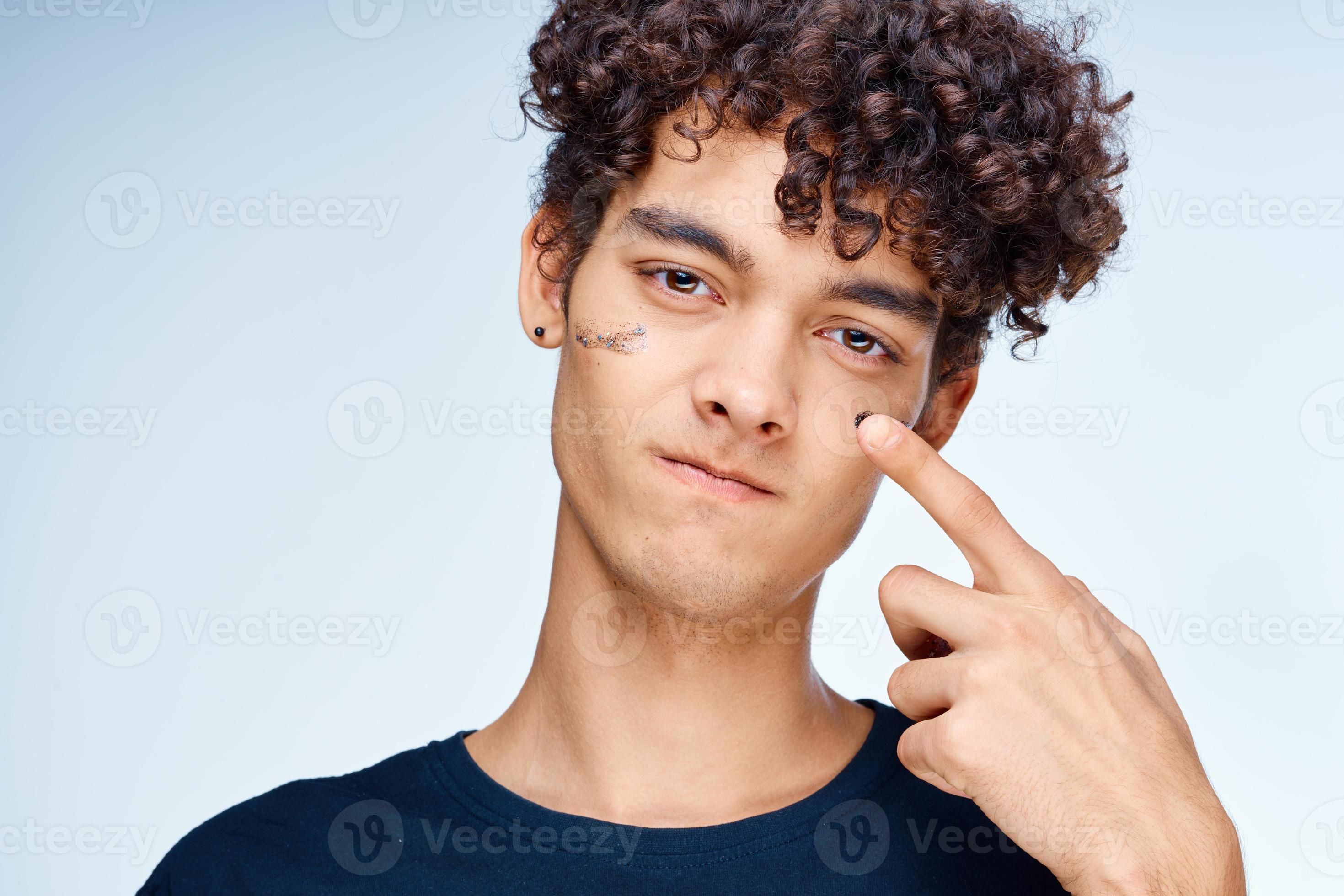handsome guy with curly hair applies a black mask on his face