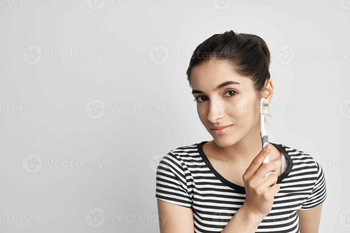 woman in a striped t-shirt toothbrush in hand light background photo