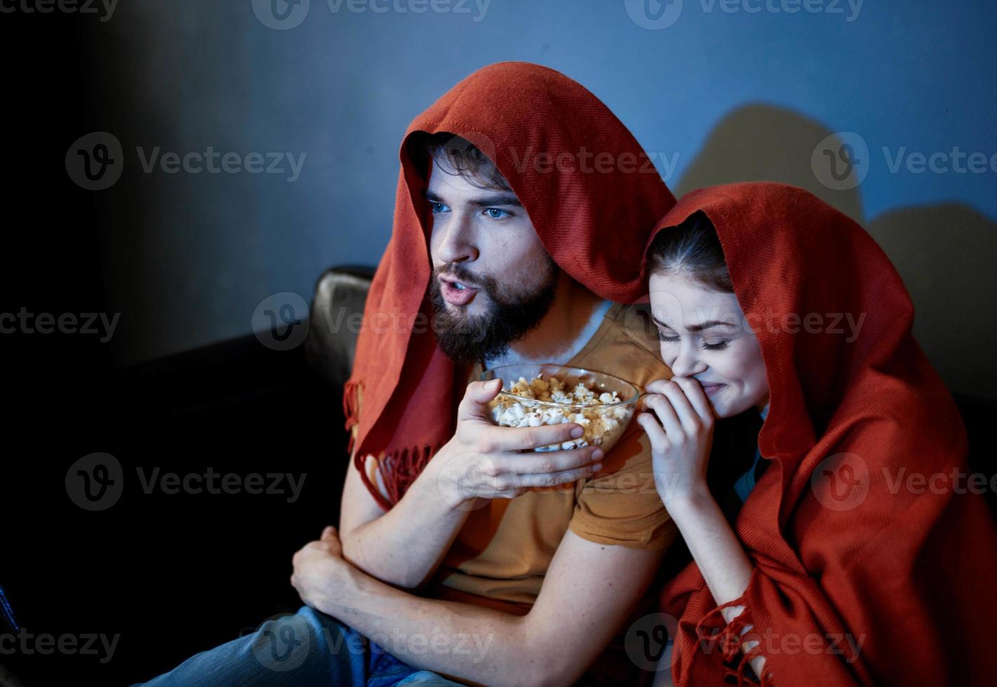 a man and a woman with a red plaid on their heads are sitting on the sofa in front of the TV indoors photo