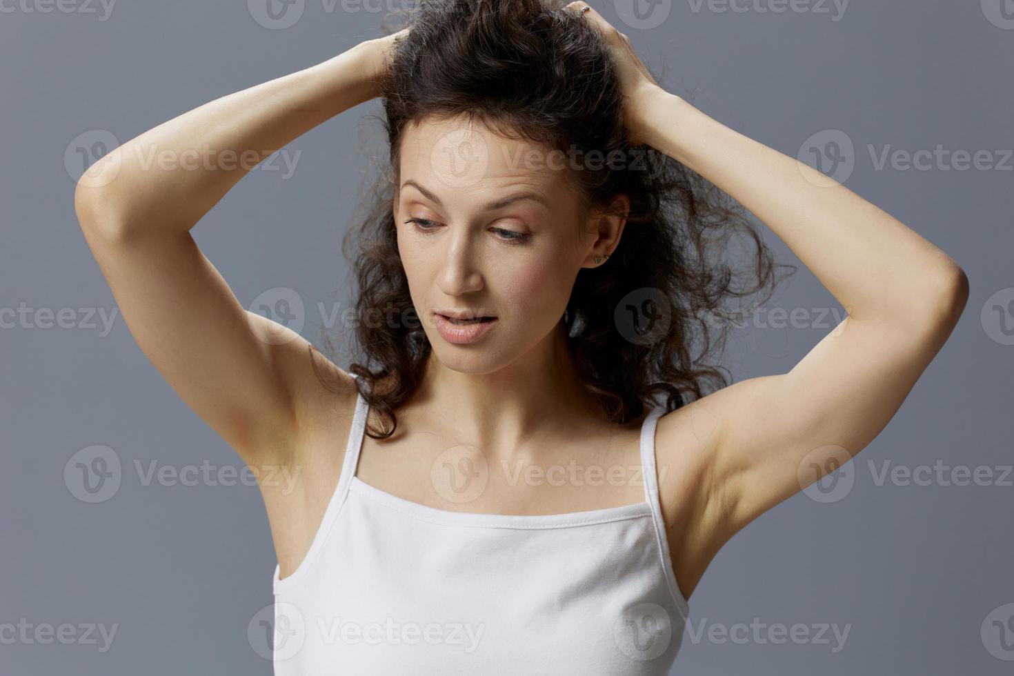 Irritated unhappy curly beautiful woman in basic white t-shirt trying to calm down hold her hair both hands posing isolated on over gray blue background. People Lifestyle Emotions concept. Copy space photo