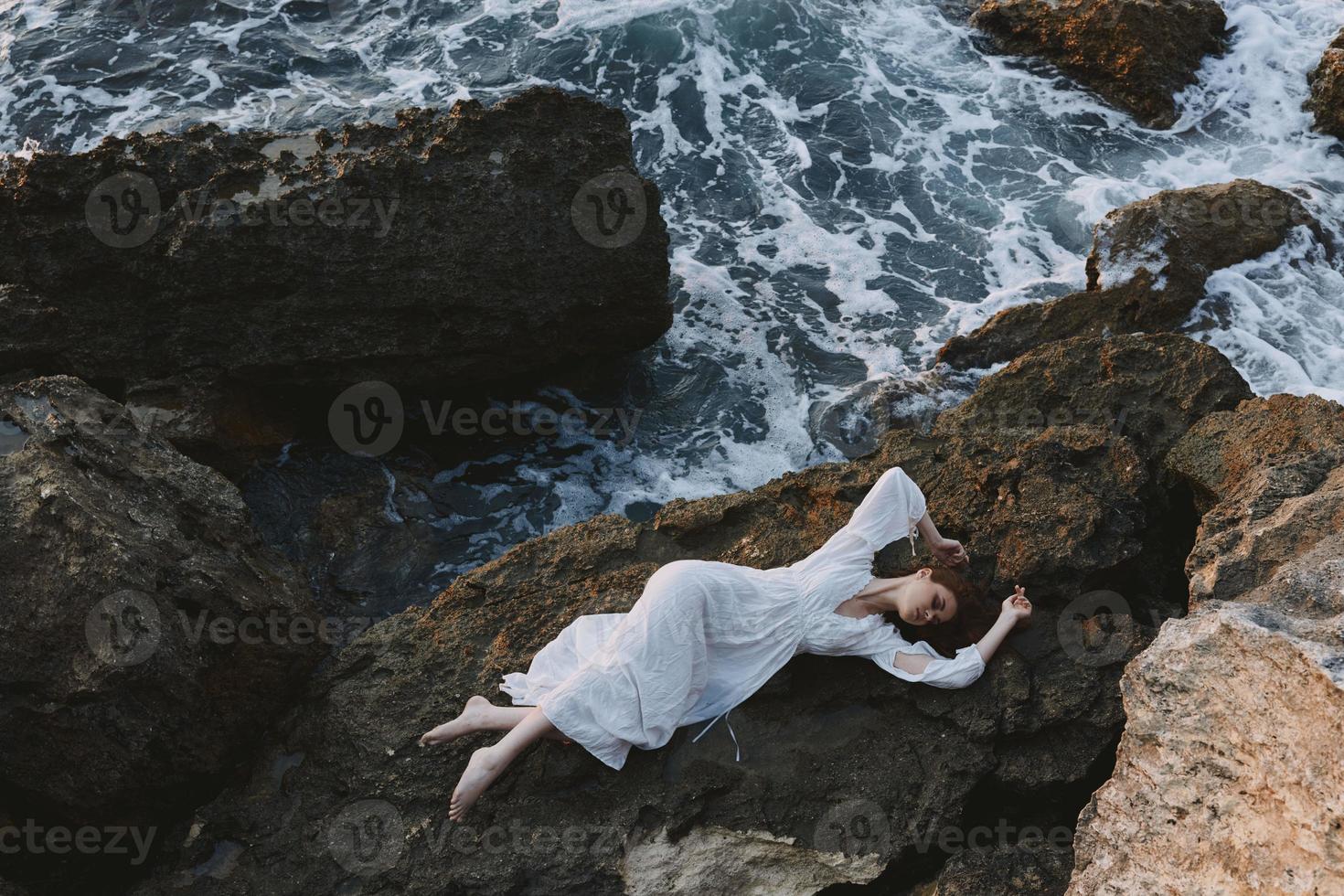 Beautiful bride lying on her back on a rocky seashore Summer vacation concept photo