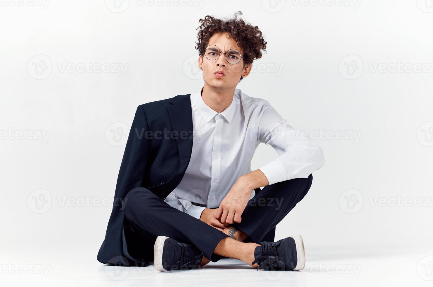 guy in a classic suit sits on the floor in a bright room glasses on the face photo