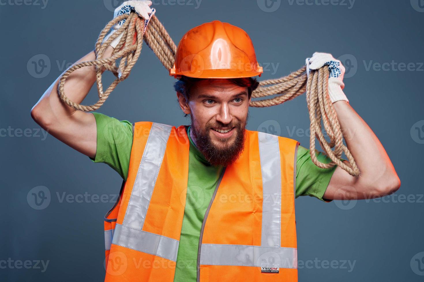 A bearded man construction worker in an orange hard hat safety rope in his hands photo