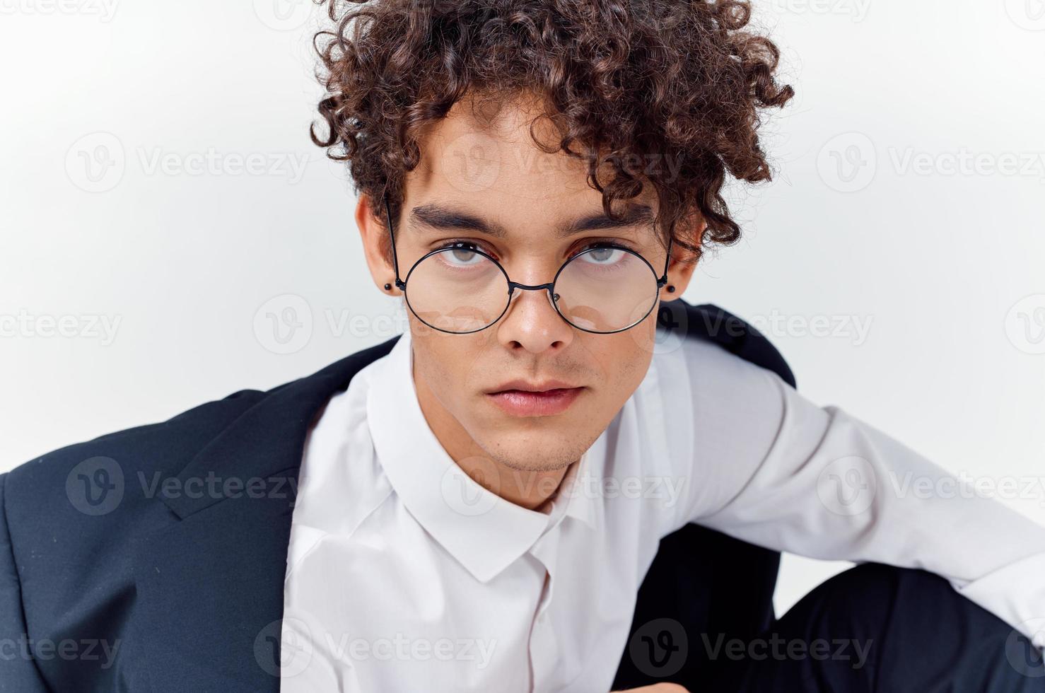 portrait of a curly-haired guy in a shirt in a jacket and glasses on a light background close-up photo