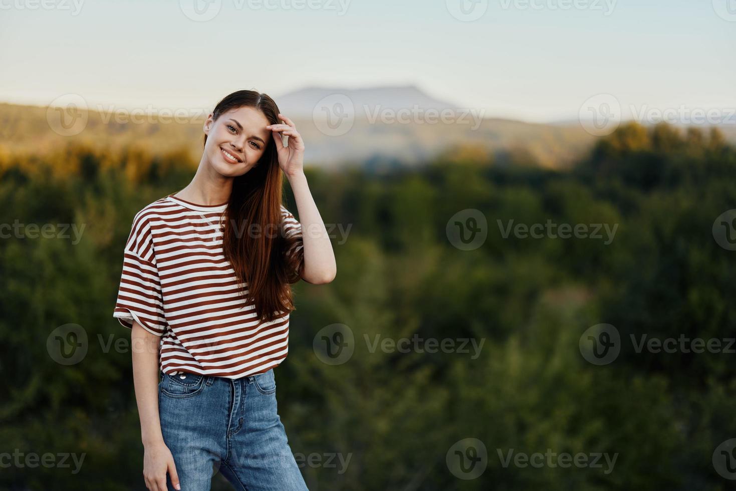 A young woman laughs and looks at the camera in simple clothes against the backdrop of a beautiful landscape of mountains and trees in autumn. Lifestyle on the move photo