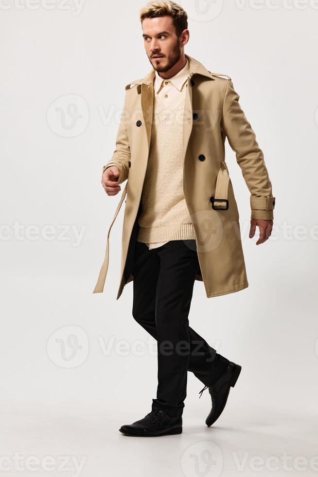 a man in a sweater coat and trousers walks to the side against a light background and gestures with his hands photo