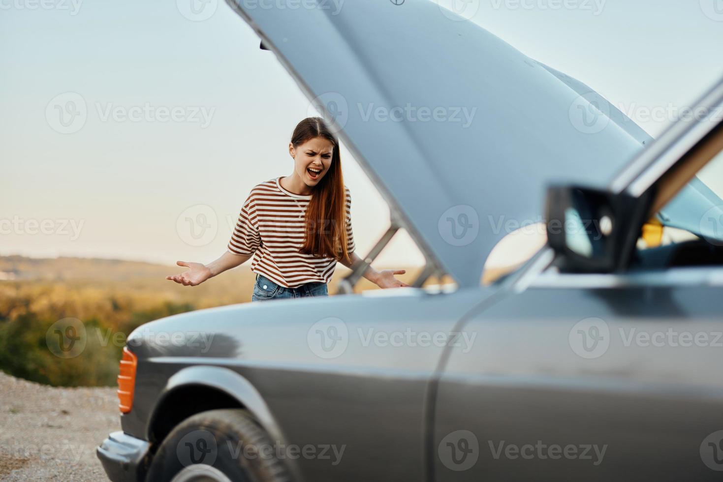 un triste mujer tiene abrió el capucha de un roto abajo coche y es mirando para el porque de el Descompostura en un la carretera viaje solo con su manos untado aparte y gritos en ira foto