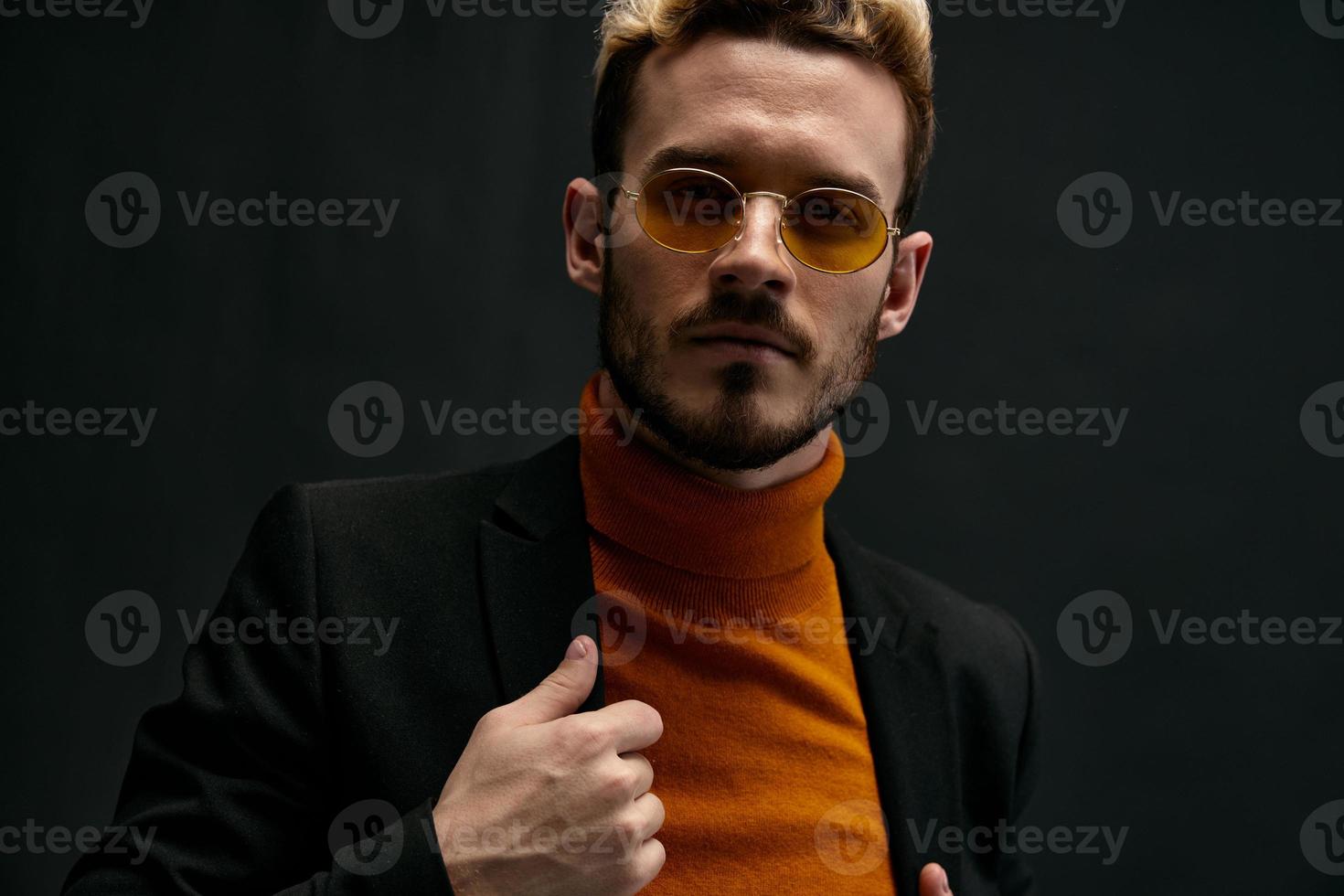 hermosa rubia con lentes y un naranja suéter negro chaqueta gesticulando con su manos oscuro antecedentes Copiar espacio foto