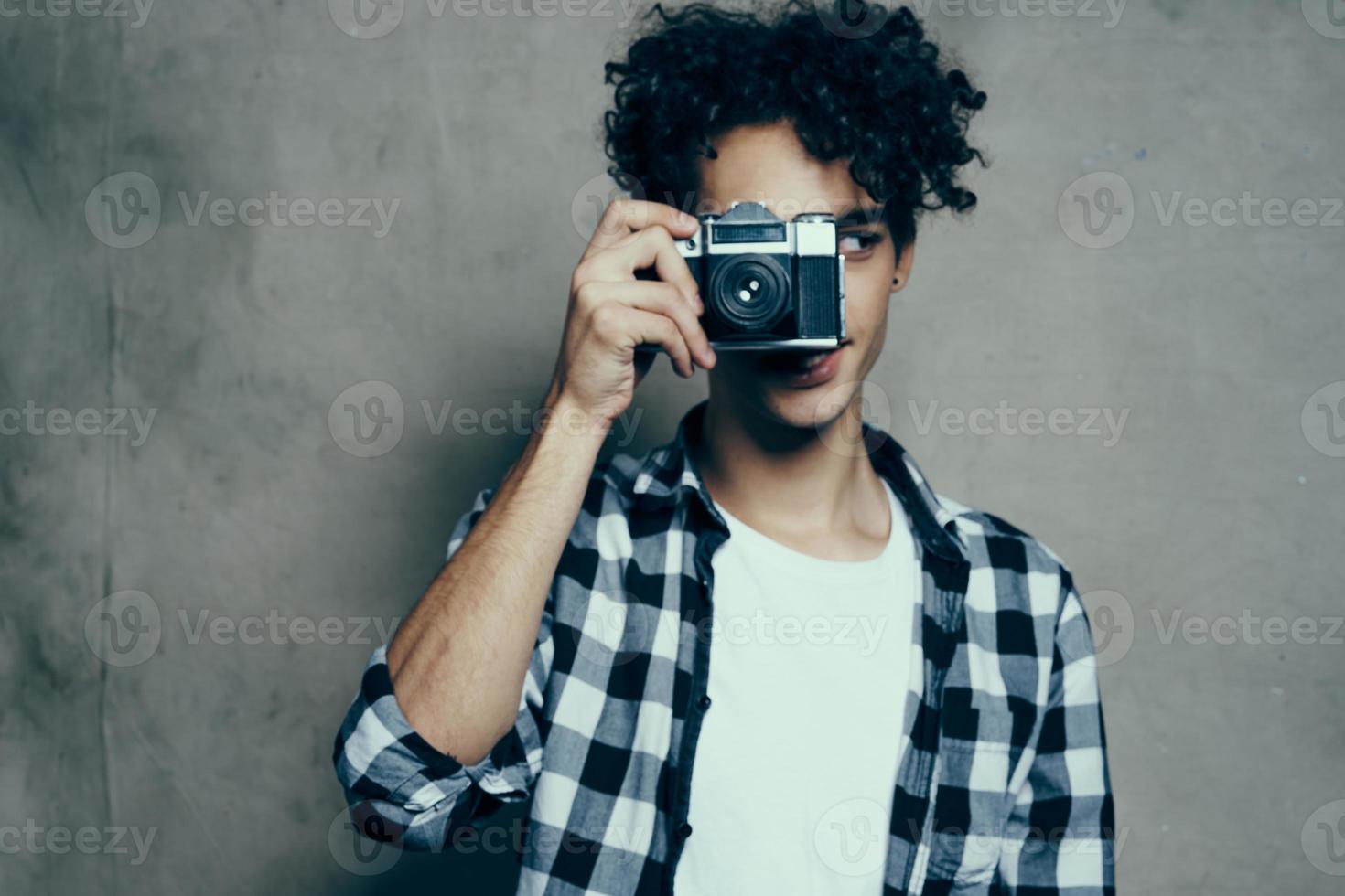 fotógrafo en un tartán camisa con un cámara en su mano en un gris antecedentes en un pasatiempo estudio habitación foto