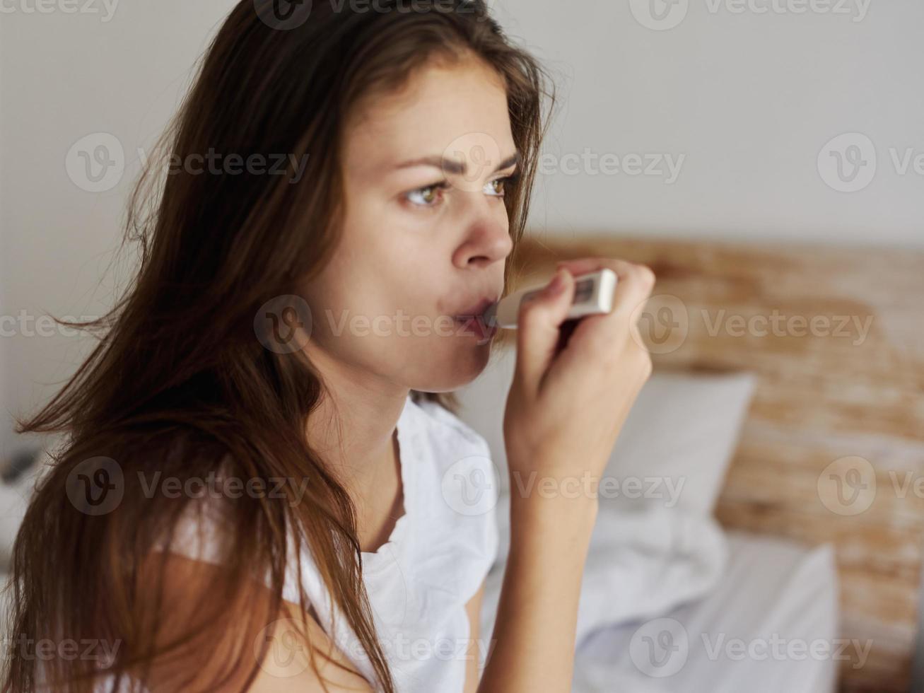 woman sitting on bed in hotel mouth thermometer checking temperature photo