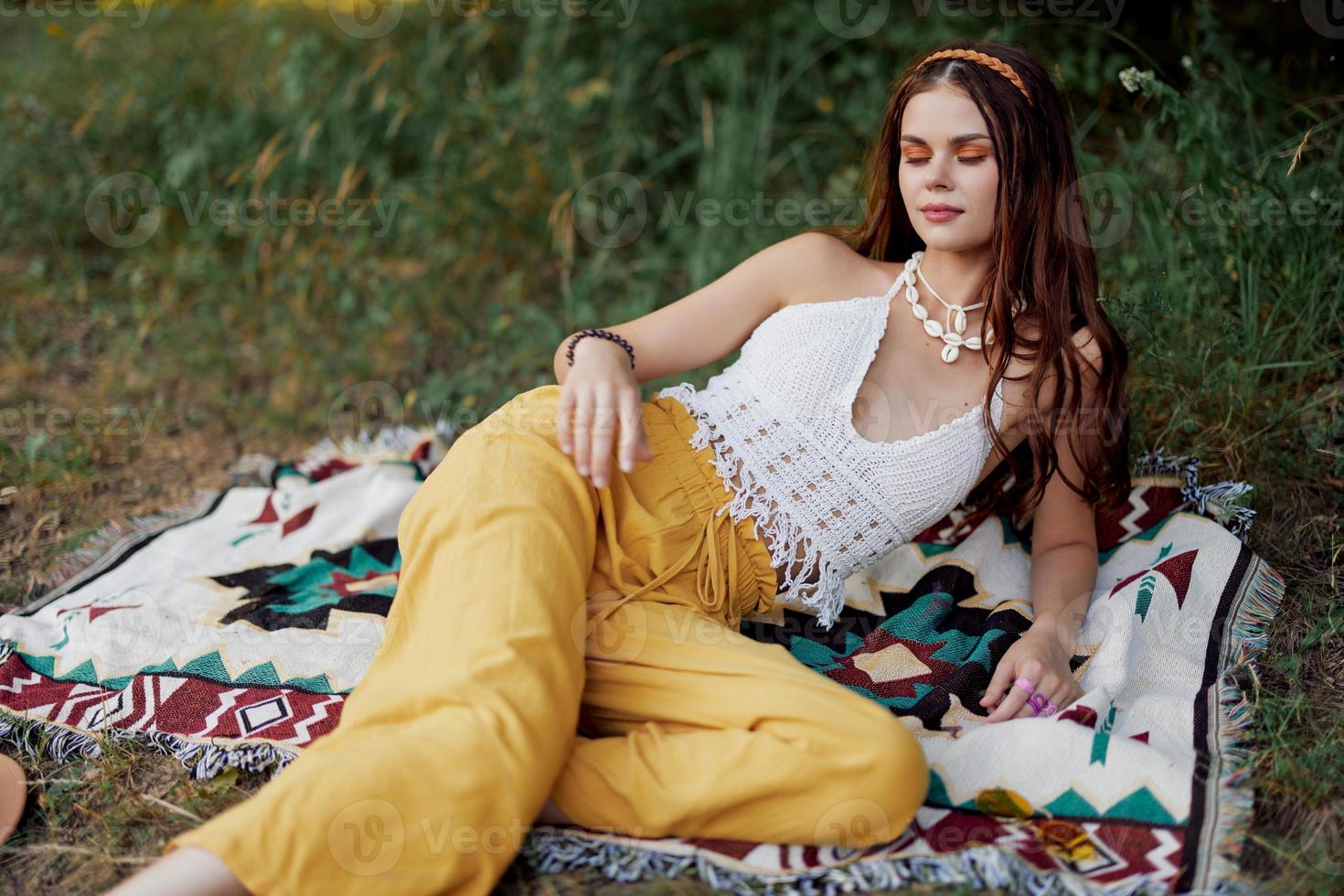 Young beautiful hippie woman lying on the ground in nature in the fall in eco clothes in yellow pants in the sunset light photo