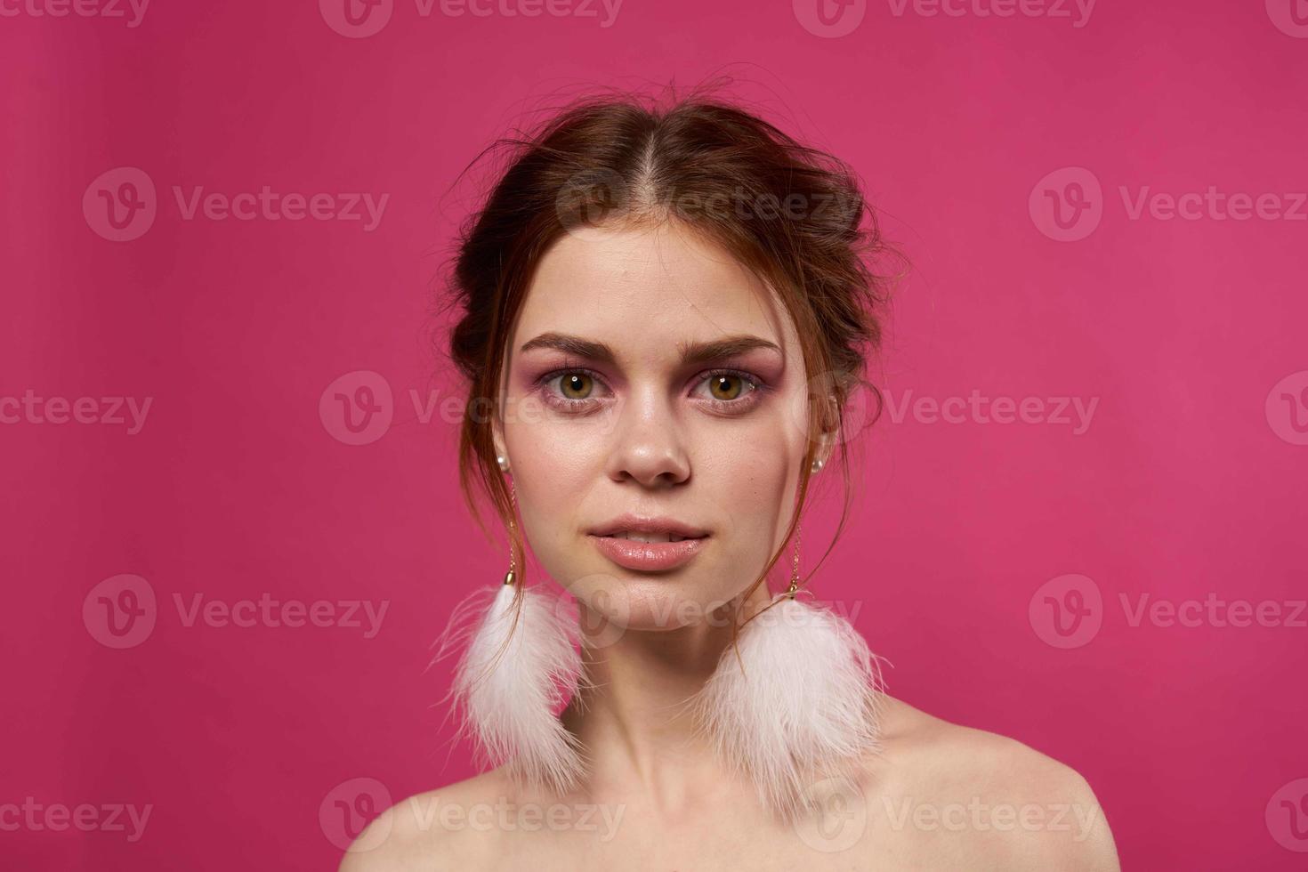 woman bare shoulders fluffy earrings bright makeup pink background photo