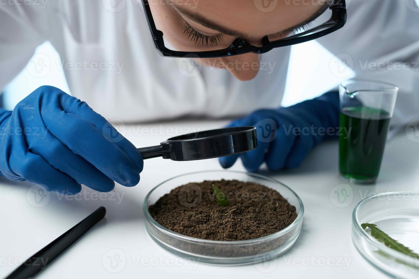 hembra laboratorio asistente mirando mediante un aumentador vaso a el suelo investigación biología foto