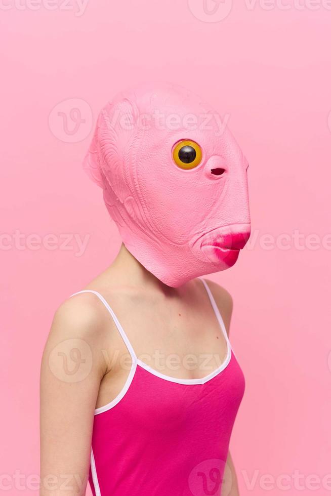 Funny crazy woman on a pink background standing in a fish head mask on a pink background, conceptual Halloween costume art photo