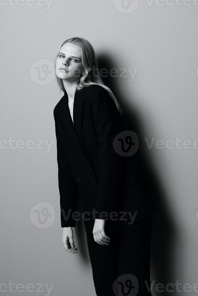 A beautiful girl in a classic suit looks into the camera leans forward posing in the studio. Black and white photo. Stylistic photography photo