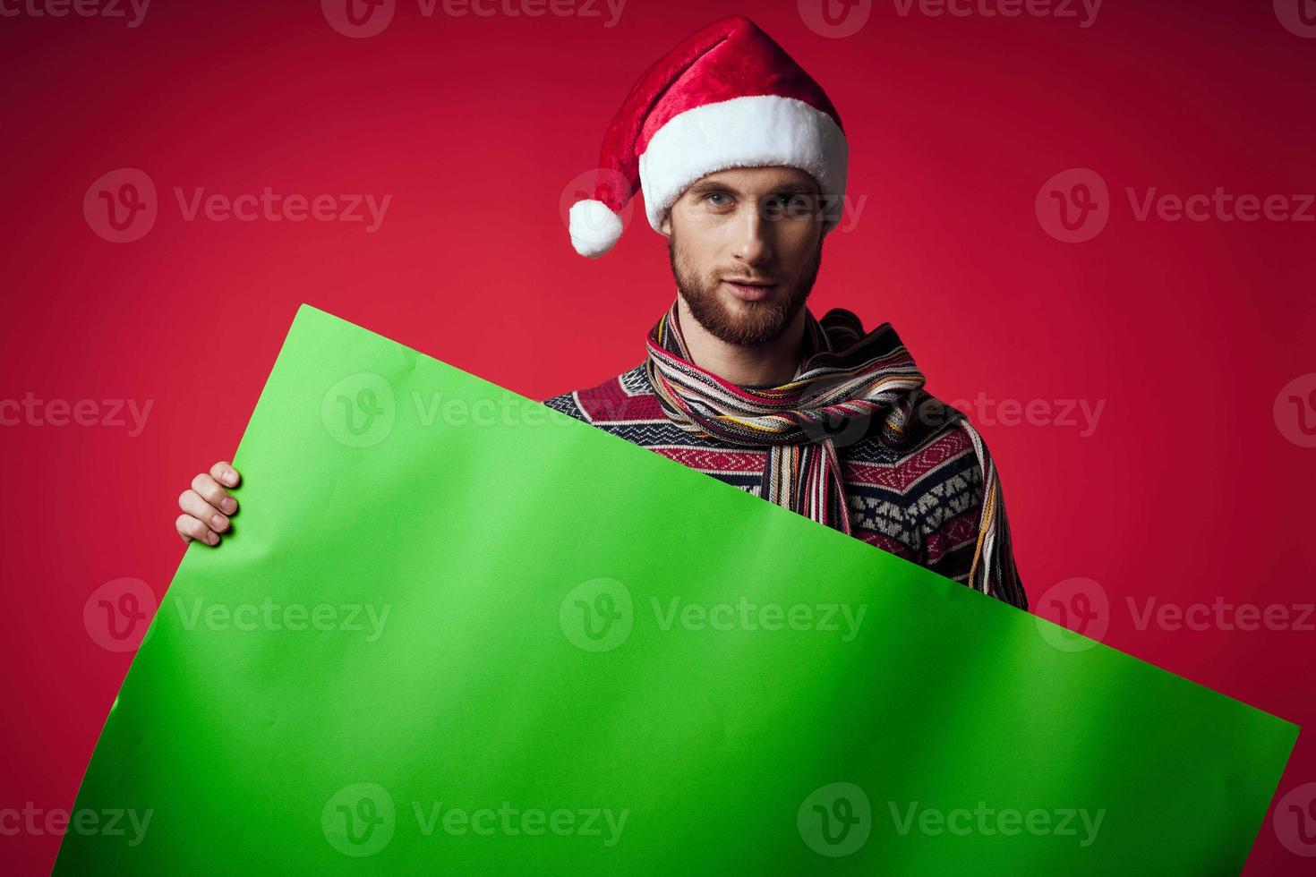 Cheerful man in a christmas hat with green mockup red background photo